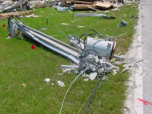 A damaged utility pole lies on the grass, surrounded by debris and scattered wires.