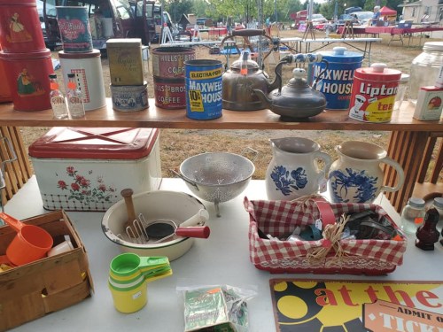 A display of vintage kitchenware, including canisters, teapots, and pitchers, at an outdoor market.