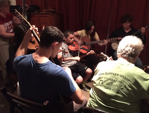 A group of musicians playing various instruments in a cozy indoor setting, focused on their performance.