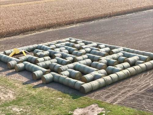 Aerial view of a maze made from round hay bales in a field, surrounded by crops and open land.