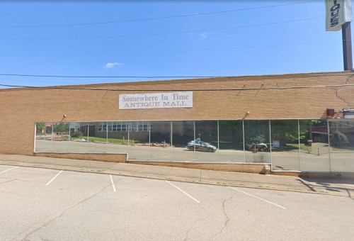 Exterior of a brick building with a sign reading "Somewhere In Time Antique Mall" and large windows reflecting the street.