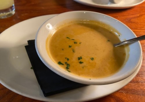 A bowl of creamy soup garnished with herbs, placed on a white plate with a black napkin underneath.