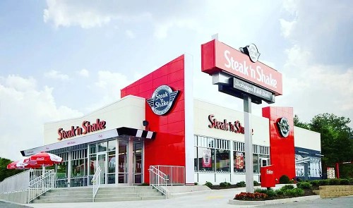 Exterior of a Steak 'n Shake restaurant with a red and white color scheme and a large sign. Cloudy sky in the background.