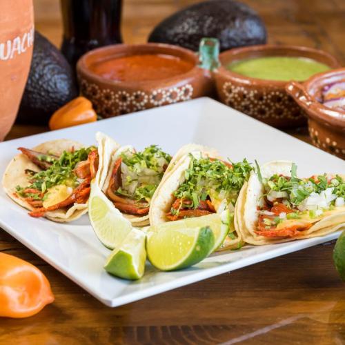 A plate of tacos topped with cilantro and onions, served with lime wedges and colorful salsas in the background.
