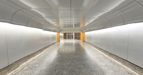 A long, empty corridor with smooth white walls and a polished floor, illuminated by soft lighting.