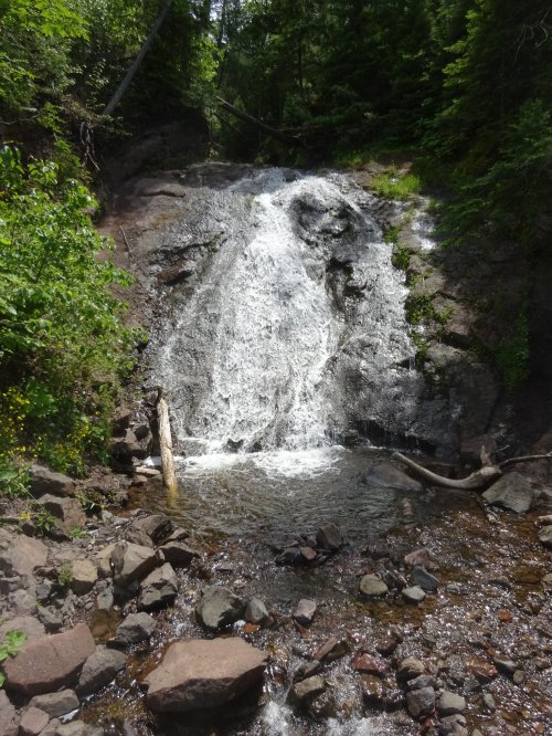 A cascading waterfall flows over rocky terrain, surrounded by lush green trees and vegetation.