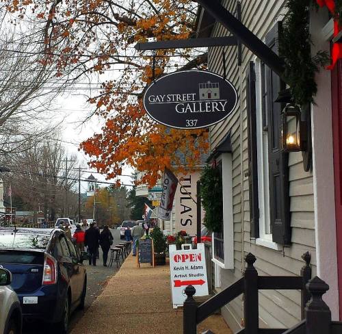A street view of Gay Street Gallery with autumn leaves, people walking, and an open sign for an artist studio.