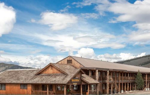 A rustic wooden lodge with a sloped roof, surrounded by a scenic sky and mountains in the background.