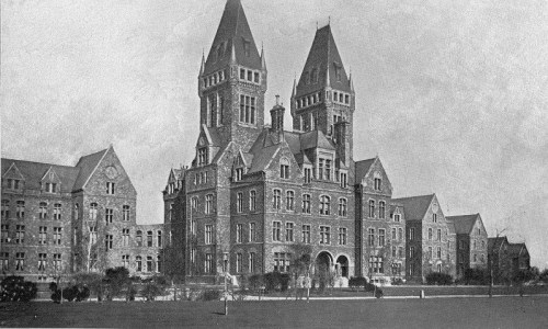 Historic building with tall towers and intricate architecture, set in a landscaped area. Black and white photo.