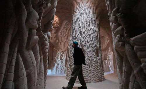 A person walks through a surreal, intricately carved cave with textured walls and towering formations.