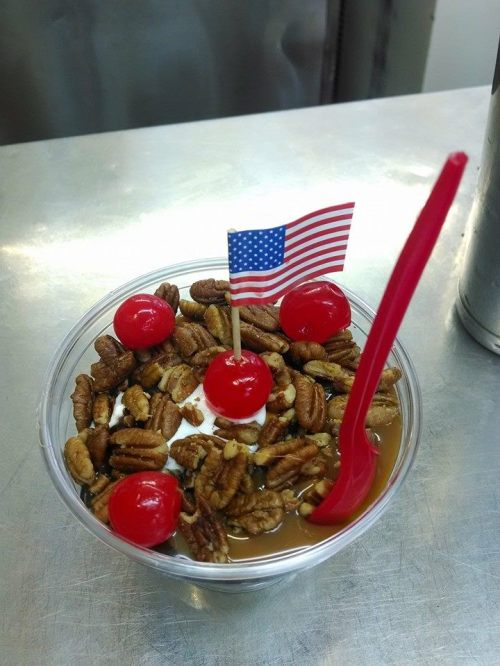 A dessert cup with whipped cream, pecans, cherries, and a small American flag on top.