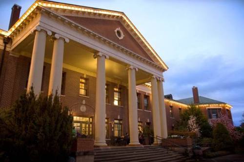 Historic building with tall columns, illuminated at dusk, surrounded by greenery and decorative lights.