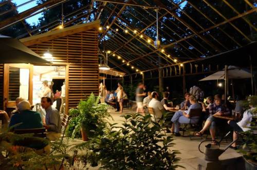 A lively outdoor dining area at night, with string lights and people enjoying their meals in a greenhouse setting.