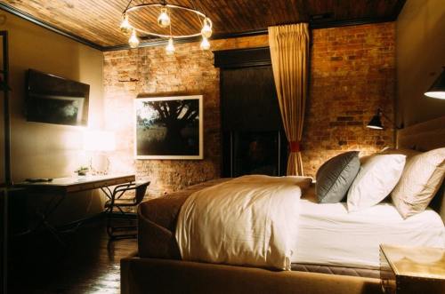 Cozy bedroom with a brick wall, a large bed, desk, and warm lighting creating an inviting atmosphere.