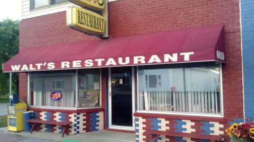 Exterior of Walt's Restaurant featuring a maroon awning, open sign, and colorful brick facade.