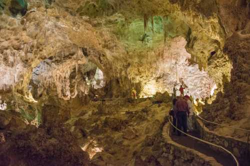 Visitors explore a stunning cave with colorful lighting, rock formations, and a winding path through the natural landscape.