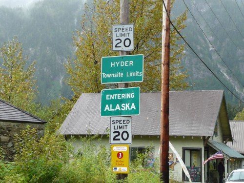 Signpost indicating "Entering Alaska" and "Hyder Townsite Limits" with speed limit of 20 mph, near a small building.