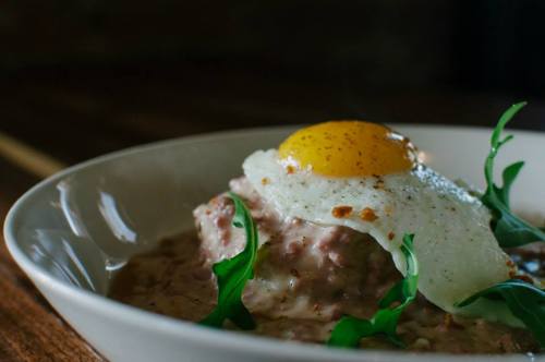 A close-up of a bowl of creamy dish topped with a fried egg and garnished with fresh greens.