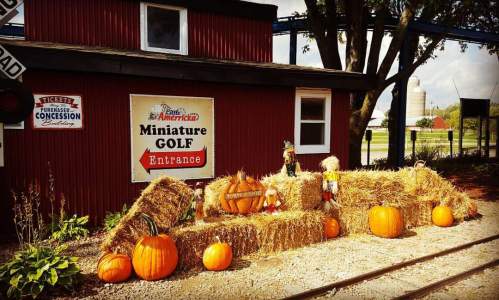 A rustic mini-golf entrance decorated with hay bales, pumpkins, and autumn-themed decor.