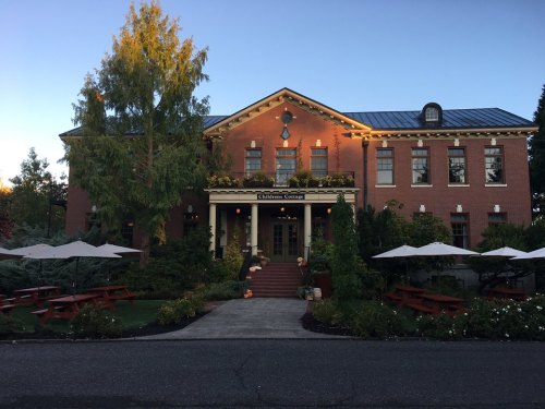 A charming brick building with a landscaped entrance, outdoor seating, and a warm evening glow.