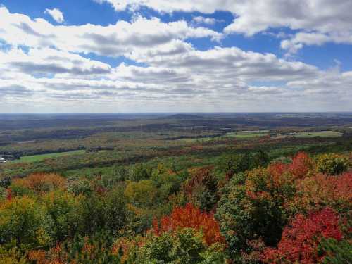 A panoramic view of a colorful autumn landscape with vibrant trees and a cloudy blue sky.