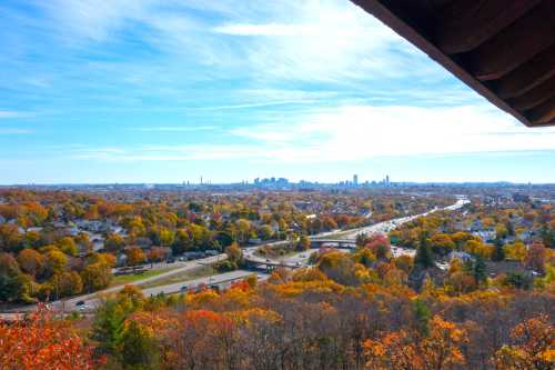 A panoramic view of a city skyline surrounded by vibrant autumn foliage and a busy highway below.