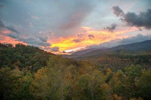 A vibrant sunset over a mountainous landscape, with colorful clouds and autumn foliage in the foreground.