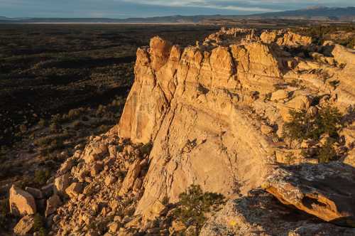 A rugged rock formation rises above a vast, green valley under a clear sky, showcasing natural beauty and geological features.