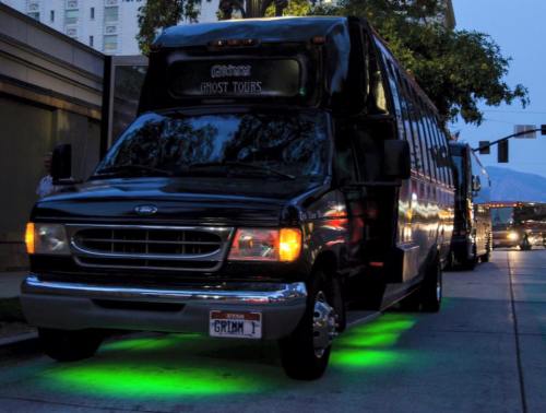 A black bus with green underglow lights parked on a street, advertising ghost tours.