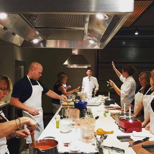 A group of people in a cooking class, preparing food in a modern kitchen with various utensils and equipment.
