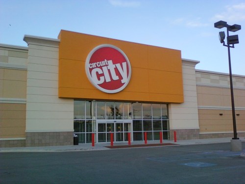 Exterior of a Circuit City store with a large logo and orange signage, featuring glass doors and a parking lot.