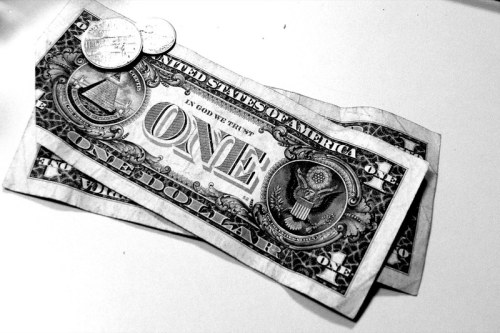 A one-dollar bill and two coins on a white surface, presented in black and white.