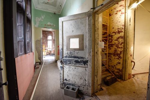 An abandoned room with peeling paint, a doorway, and a ladder leading to another area, showcasing signs of decay.