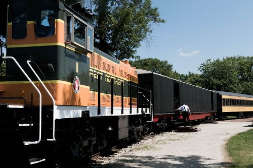 A vintage train engine parked beside passenger cars, with a person boarding on a sunny day.