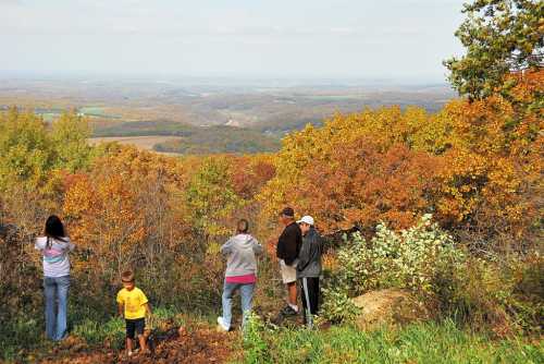 A group of people enjoying a scenic view of autumn foliage and rolling hills from a lookout point.