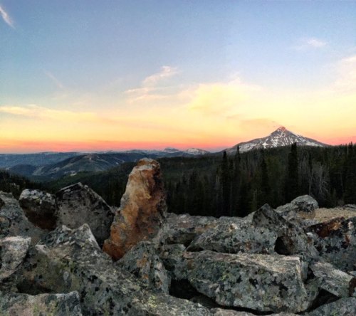 A scenic view of mountains at sunset, with rocky foreground and a colorful sky transitioning from orange to blue.
