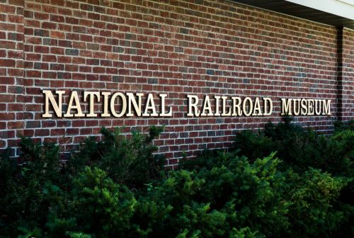Sign for the National Railroad Museum on a brick wall, surrounded by green shrubs.