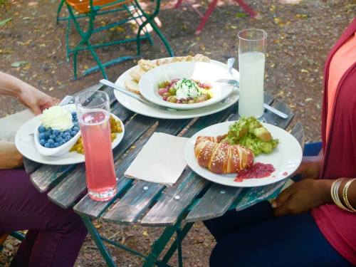 A table outdoors with two plates of food, drinks, and desserts, surrounded by greenery and colorful chairs.