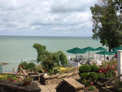 A serene lakeside view with green umbrellas, flower gardens, and a cloudy sky over calm waters.