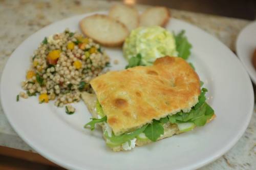 A plate with a sandwich, salad, and a side of couscous and two small bread rolls.