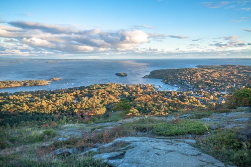 A scenic view from a mountain overlooking a colorful autumn landscape and a calm bay with boats.