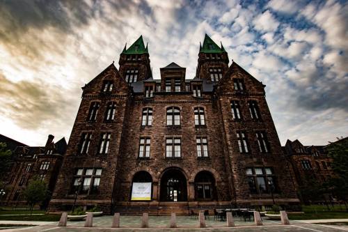 Historic stone building with green-tipped towers, set against a dramatic sky.