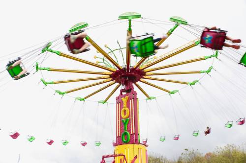 A colorful swing ride spins in the air, with riders in seats flying outward against a cloudy sky.