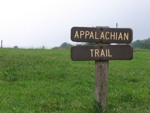 Signpost for the Appalachian Trail, set against a grassy landscape under a cloudy sky.