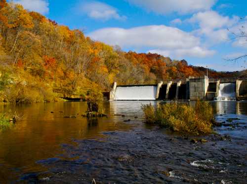 A serene river scene with a dam, surrounded by autumn foliage and a clear blue sky.