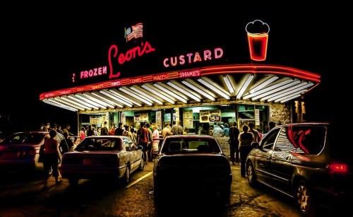 A vibrant neon-lit ice cream stand with a crowd of people enjoying frozen custard on a warm evening.