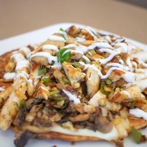 A plate of loaded nachos topped with grilled chicken, mushrooms, green peppers, and drizzled with creamy sauce.