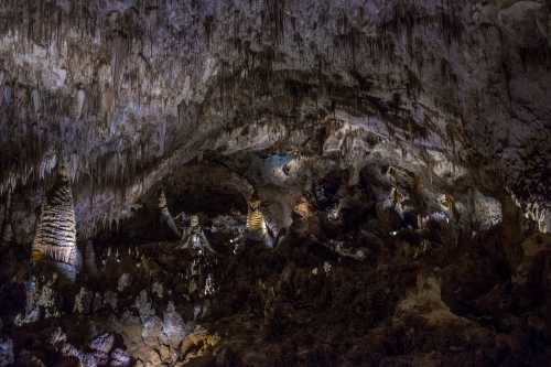 A dimly lit cave interior featuring stalactites and stalagmites, with intricate rock formations and shadows.