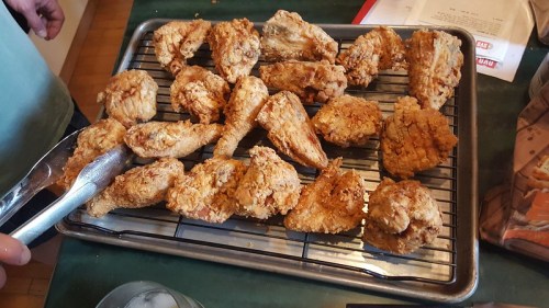 A tray of golden-brown fried chicken wings on a cooling rack, with tongs resting on the side.