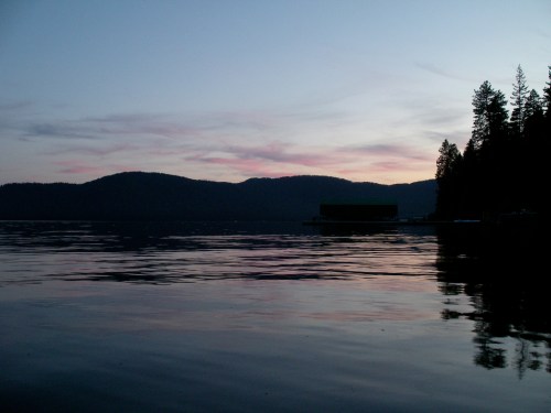 Serene lake at dusk, with mountains in the background and a colorful sky reflecting on the water's surface.